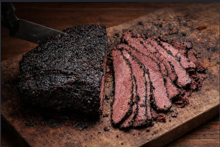 Peça de pastrami com crosta temperada e fatias sobre tábua de madeira